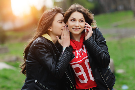 Two pretty and happy young woman using the mobile phone in the park.