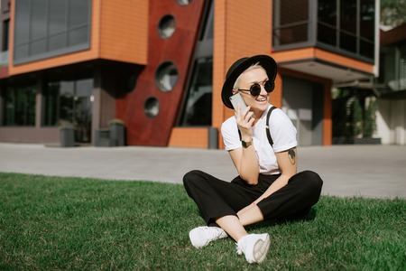 Attractive successful female person dressed in stylish outfit talking on mobile phone with friends while walking at urban setting.Cheerful hipster girl enjoying leisure time at street with gadget.の写真素材