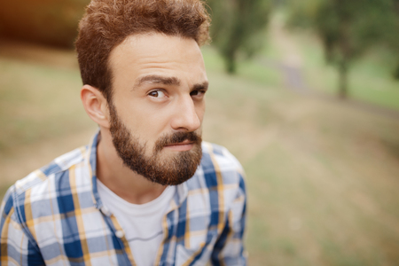 Attractive curious young bearded hipster posing in the park.の写真素材