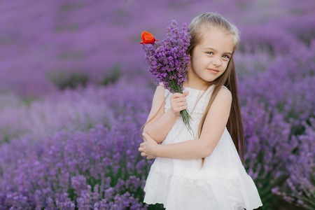 Happy cute little girl in lavender field holding bouquet of purple flowers.の写真素材