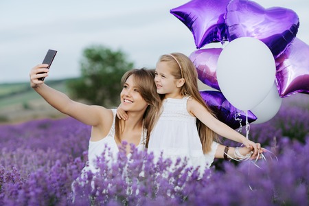 Mom and Daughter make selfie on smartphone in the lavender field. Family love concept.の写真素材