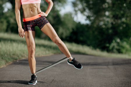 Young sporty woman doing exercises with rubber band outdoor.