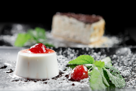 Photo of italian panna cotta dessert with strawberry sirup and mint leaf on the black wooden background.の写真素材