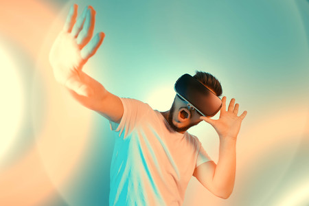 Photo of shocked bearded man trying VR headset and exploring another world on the colorful...