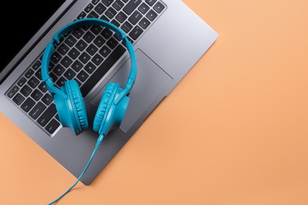 Photo of stylish modern computer or notebook and blue cyan headphones over beige background.の写真素材