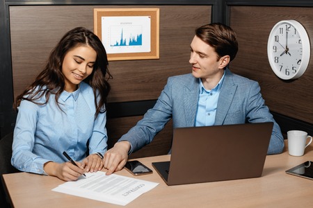 Photo of two colleagues working together with laptop and business documents in modern office....