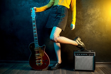 Close-up photo of young hipster woman legs and red guitar in neon lights. Rock musician is playing electrical guitar. 90s style concept.の写真素材