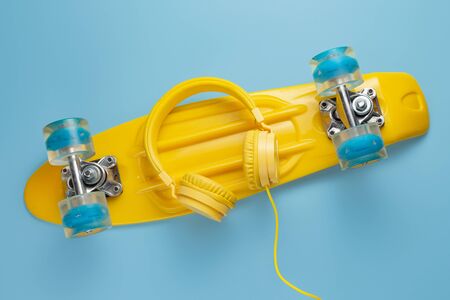 Yellow headphones and skateboard or pennyboard on blue background. Music concept.