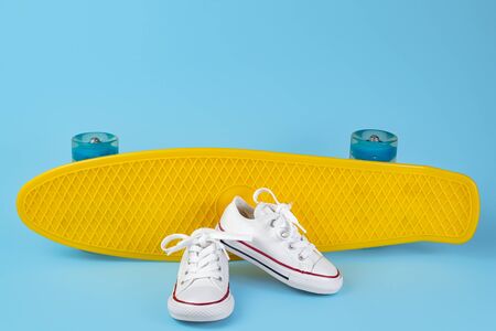 White sneakers in front of skateboard or penny board over blue background.の写真素材