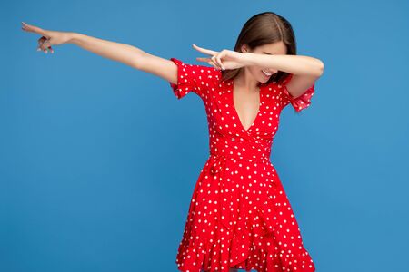 Young woman with bright smile in red casual dress dubbing over blue background.の写真素材