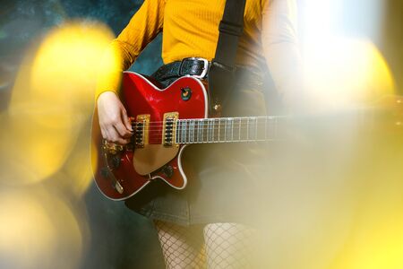 Close-up photo of young hipster woman legs and red guitar in neon lights. Rock musician is playing electrical guitar. 90s style concept.の写真素材