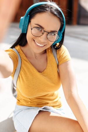 Funny brunette young woman with bright smile dressed in casual clothes take selfie with smartphone in the street.の写真素材