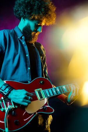 Close-up photo of hipster man with red guitar in neon lights. Rock musician is playing electrical guitar.の写真素材