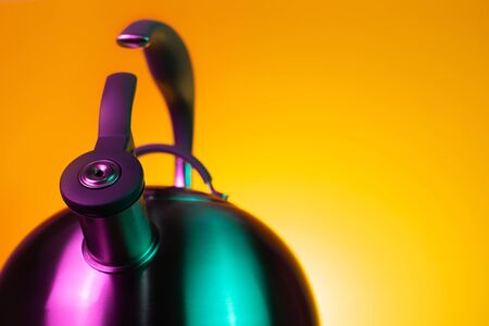 Close-up photo of stainless steel kettle in neon light over yellow background.の写真素材