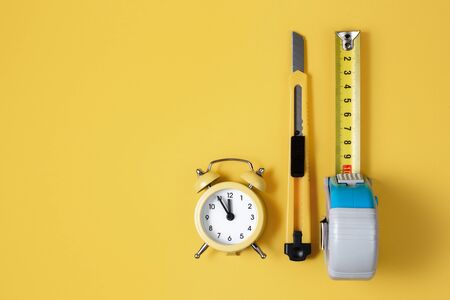 Measuring tape, cutter knife and clock isolated over yellow bakground. Carpenter and Construct concept.の写真素材