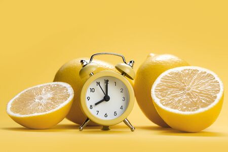 Lemon fruit slice and whole lemons on yellow background. Yellow alarm clock in front of lemons.の写真素材