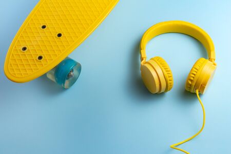 Yellow headphones and skateboard or pennyboard on blue background. Music concept.