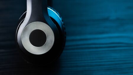 Black headphone on dark wooden background. Stylish wireless headset in neon light.