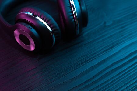 Black headphone on dark wooden background. Stylish wireless headset in neon light.