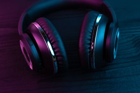 Black headphone on dark wooden background. Stylish wireless headset in neon light.の写真素材