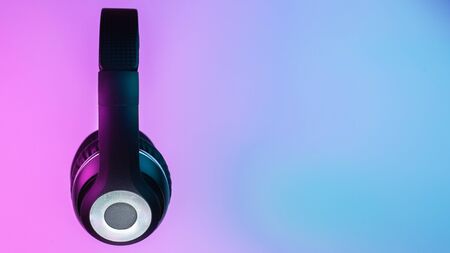 Retro 90s style photo of black stylish wireless headphone in neon lights.