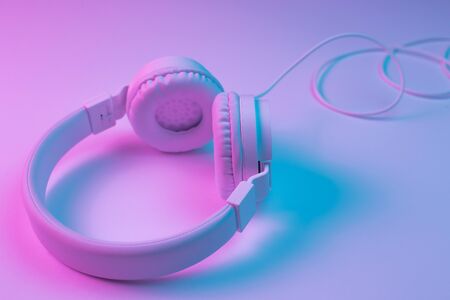 Retro 90s style photo of white stylish wireless headphone in neon lights. Music concept.