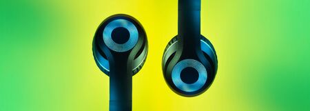 Retro 90s style photo of black stylish modern wireless headphone in neon lights over colorful...
