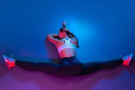 Attractive young slim gymnast woman in sports clothing stretching on the floor in neon lights. Top view.の写真素材