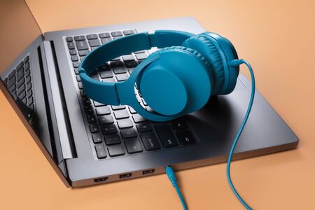 Photo of stylish modern computer or notebook and blue cyan headphones over beige background.の写真素材