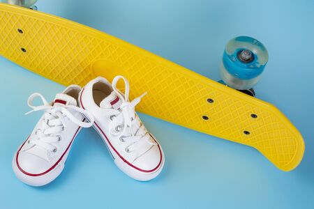 Photo of white sneakers on the skateboard or penny board over blue background.