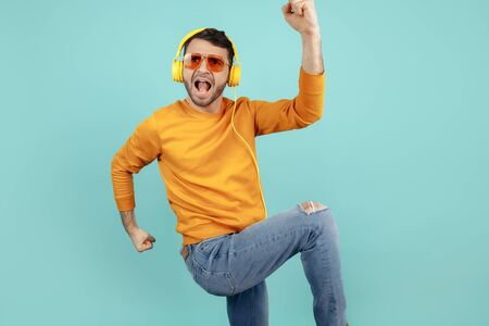 Excited bearded young man wearing sunglasses listening to music celebrate success over cyan background.の写真素材
