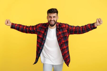 Excited bearded hipster young man in plaid shirt celebrate over yellow background. Look in camera.の写真素材
