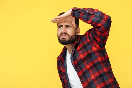 Trendy bearded hipster young man in plaid shirt looking far away over yellow background.の写真素材