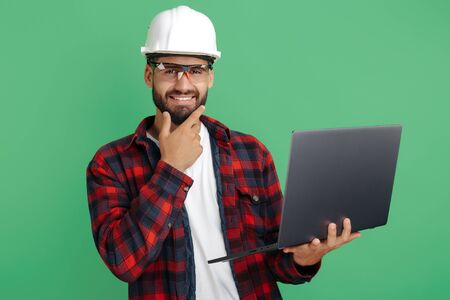 Handsome bearded engineer or constructor man in casual outfit with computer over green background.の写真素材