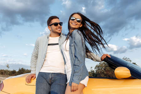 Gleeful young couple staying beside a yellow convertible car. Freedom, travel and love concept.