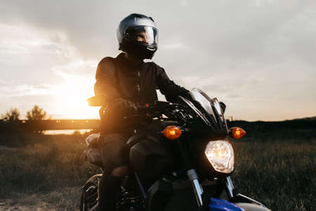 Close-up photo of biker sitting on motorcycle in sunset on the country road.の写真素材