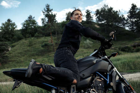 Close-up photo of biker sitting on motorcycle in sunset on the country road.