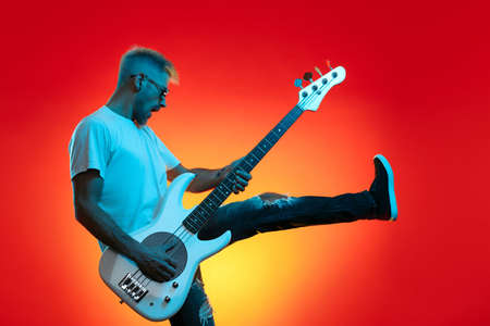 Screaming hipster man play white bass guitar in neon lights. Rock music concept.の写真素材