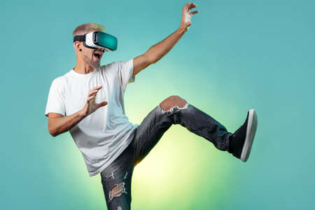 Screaming bearded hipster man with blonde hair wearing virtual reality goggles in studio in neon...