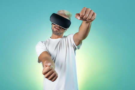 Surprised bearded hipster man with blonde hair wearing virtual reality goggles in studio in neon...
