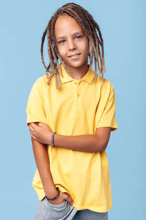 Portrait of timid little boy with african dreads posing over blue background.の写真素材