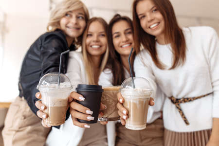 Cheerful four young women friends having coffee break while relaxing at the cafe indoors. Focus on cups.の写真素材