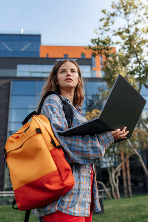 Stylish young blonde hipster woman student with backpack use notebook or computer at university.