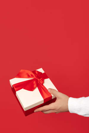 Close-up image of man hands holding gift box over red background. Christmas and New Year concept.の写真素材