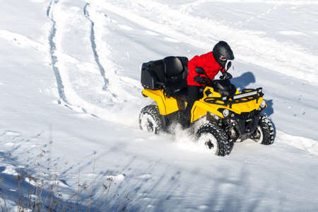 Young man driver driving his ATV 4wd quad bike stand in heavy snow with deep wheel track.