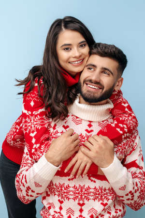 Lovely couple dressed in Christmas sweaters hugging over blue background.の写真素材