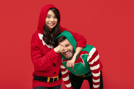 Cheerful couple dressed in Christmas funny sweaters having fun over red background.の写真素材