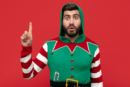 Shocked hipster man dressed in Christmas sweater pointing finger up over red background.の写真素材