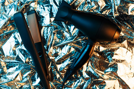 Hair dryer and hair straightener in neon lights on the foil with shiny crumpled surface background. 80s and 90s style.の写真素材