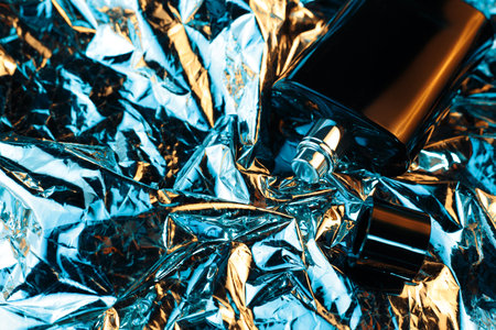 Black bottle of men perfume in neon lights on the foil with shiny crumpled surface background. 80s and 90s style.の写真素材